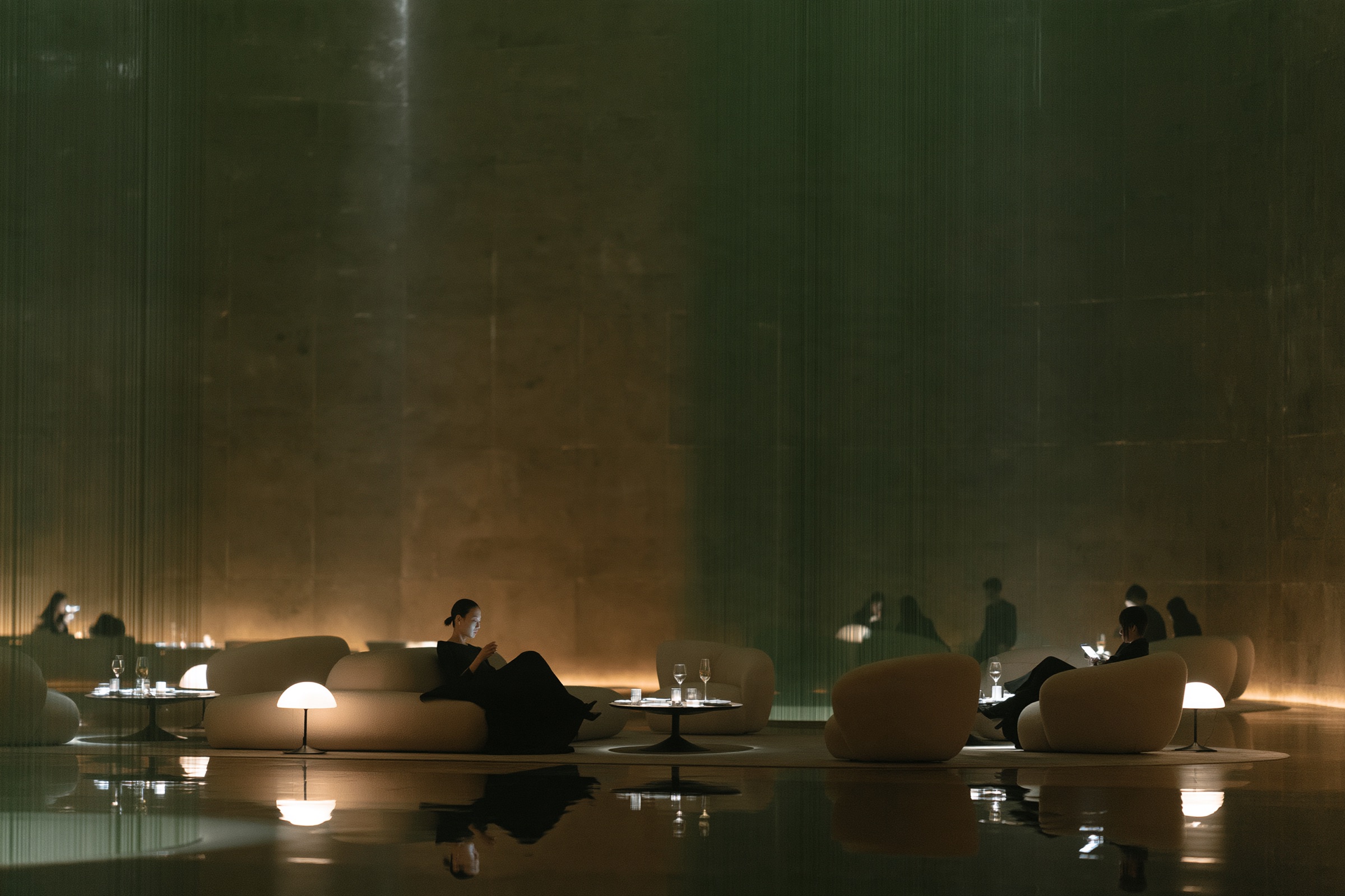 Members in a low-lit lounge of curved sofas and small lamps beside a dark pool
