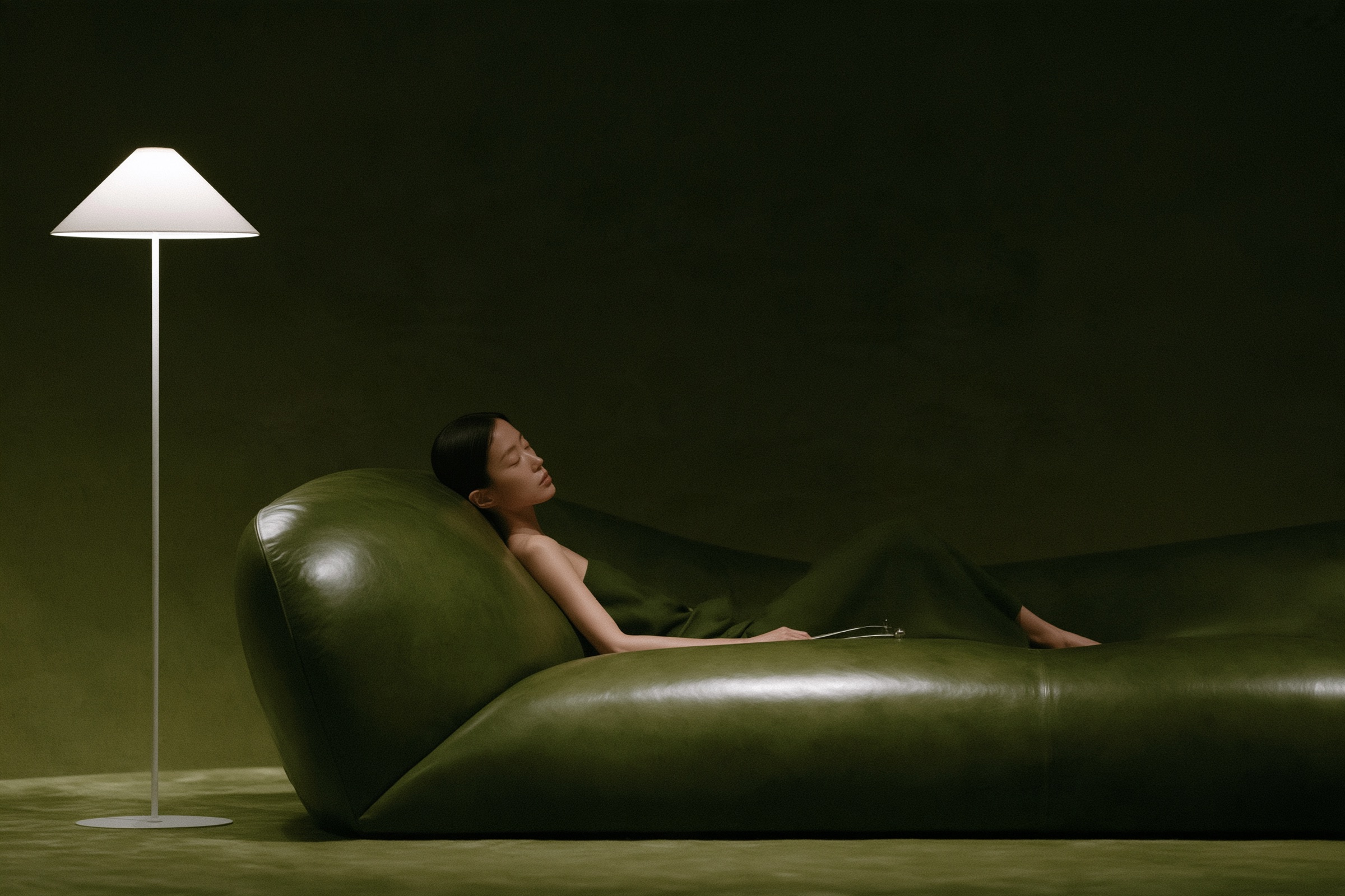 A woman resting on a deep green leather lounger under a floor lamp